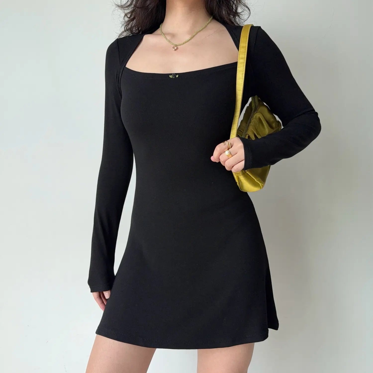 Model front pose carrying yellow shoulder bag black square halter long sleeve bodycon mini dress