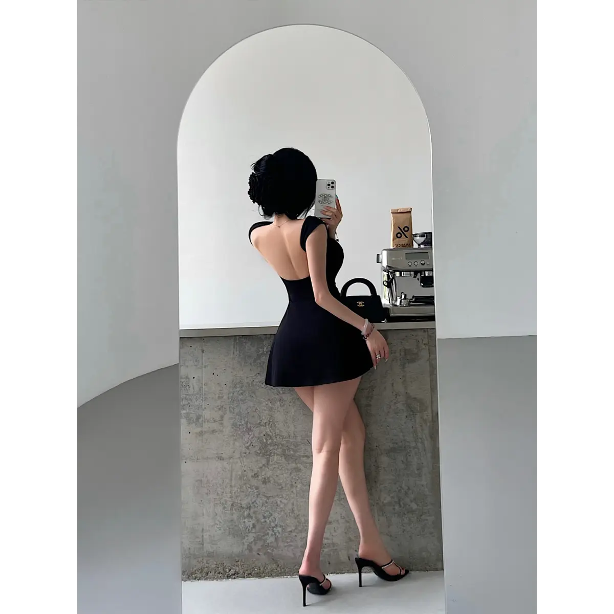 Back view of a woman wearing a black square-neck, low-back fit-and-flare mini dress taking a mirror selfie.