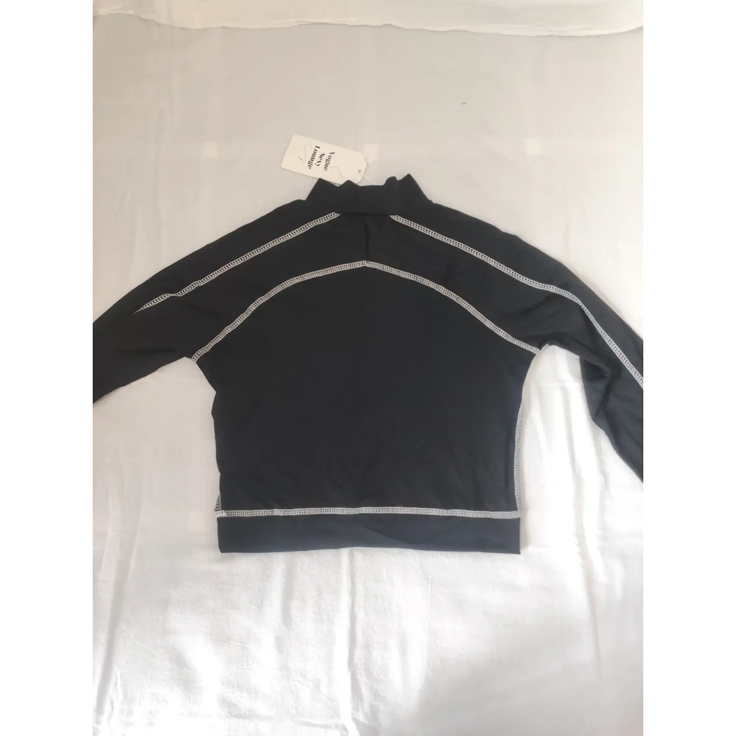 Flat lay back view black long sleeve crop top with white contrast stitching and clothing hang tag