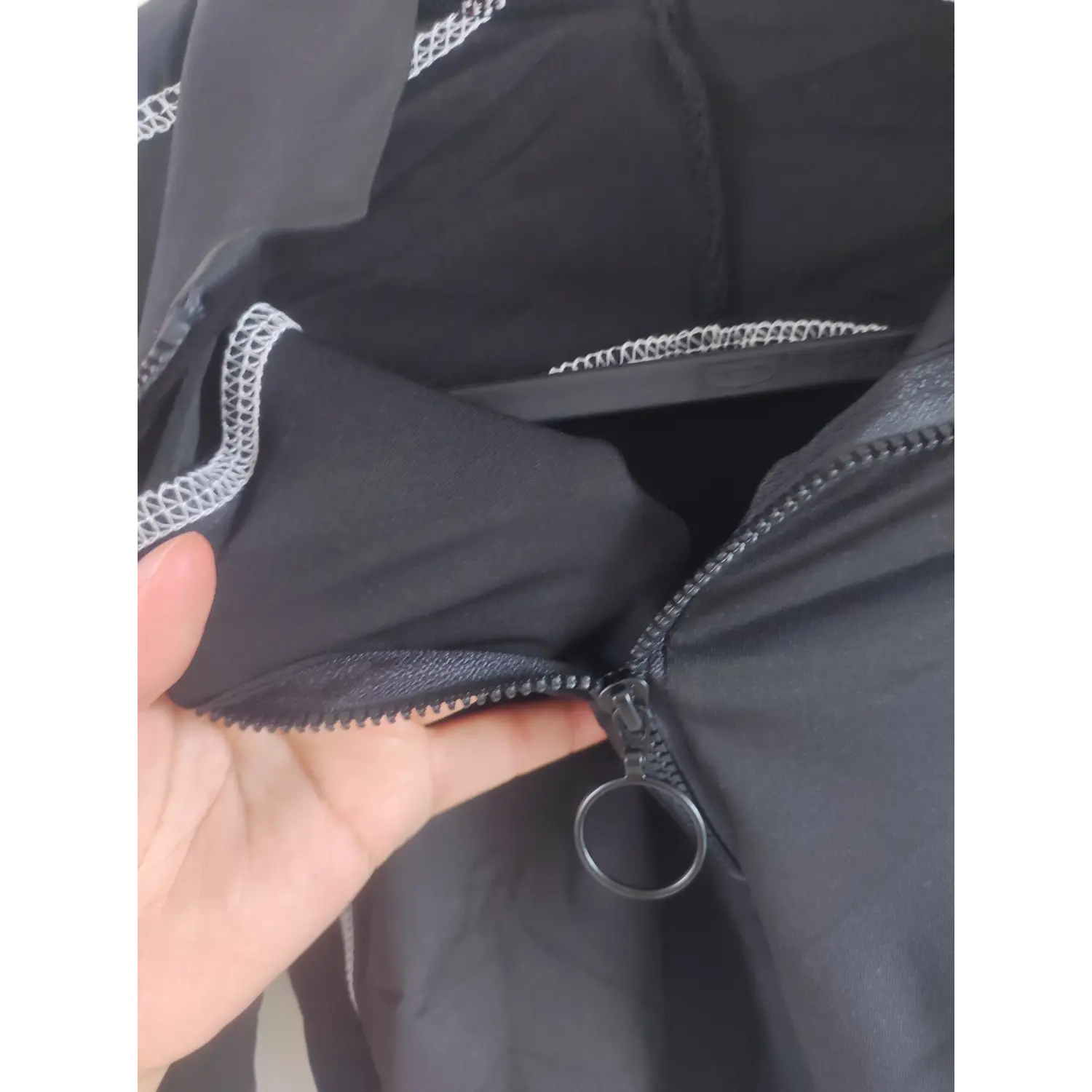 Close-up shot of ring pull half zipper and white contrast stitching on black long sleeve cropped top