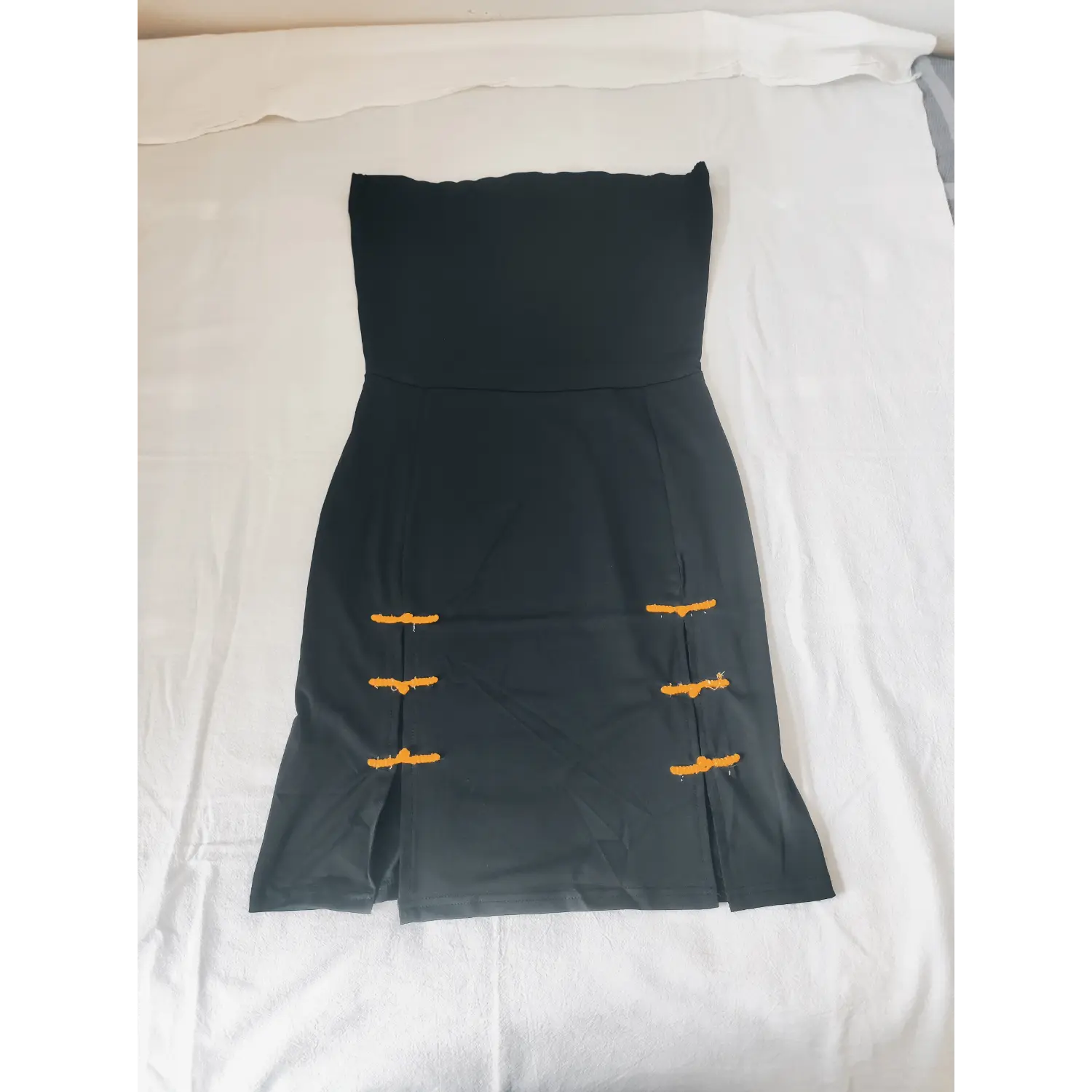 Flat lay black strapless bodycon mini dress with yellow chinese knot side slits | Detail