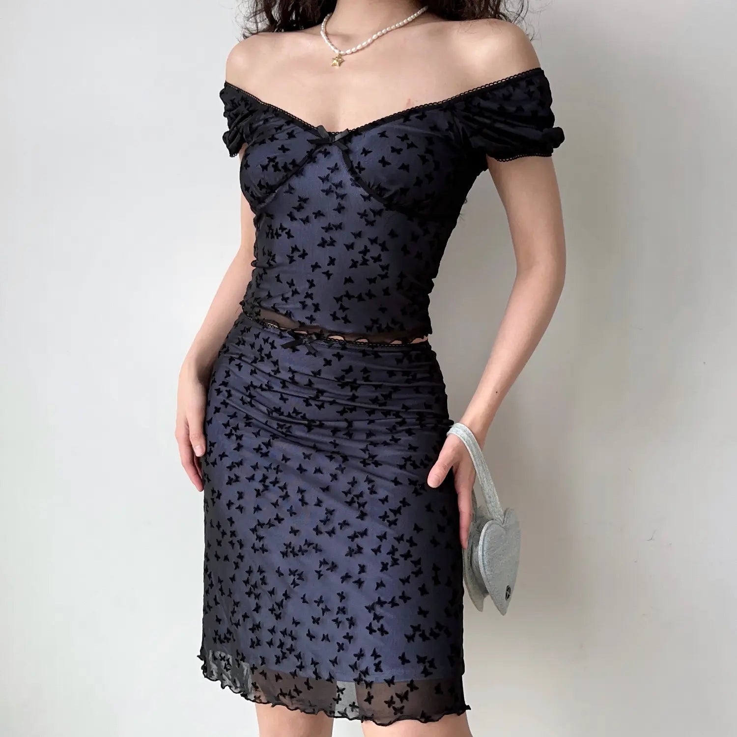 Front full length studio photo black mesh two piece outfit, sweetheart off shoulder top, midi ruched skirt with allover flock butterfly pattern