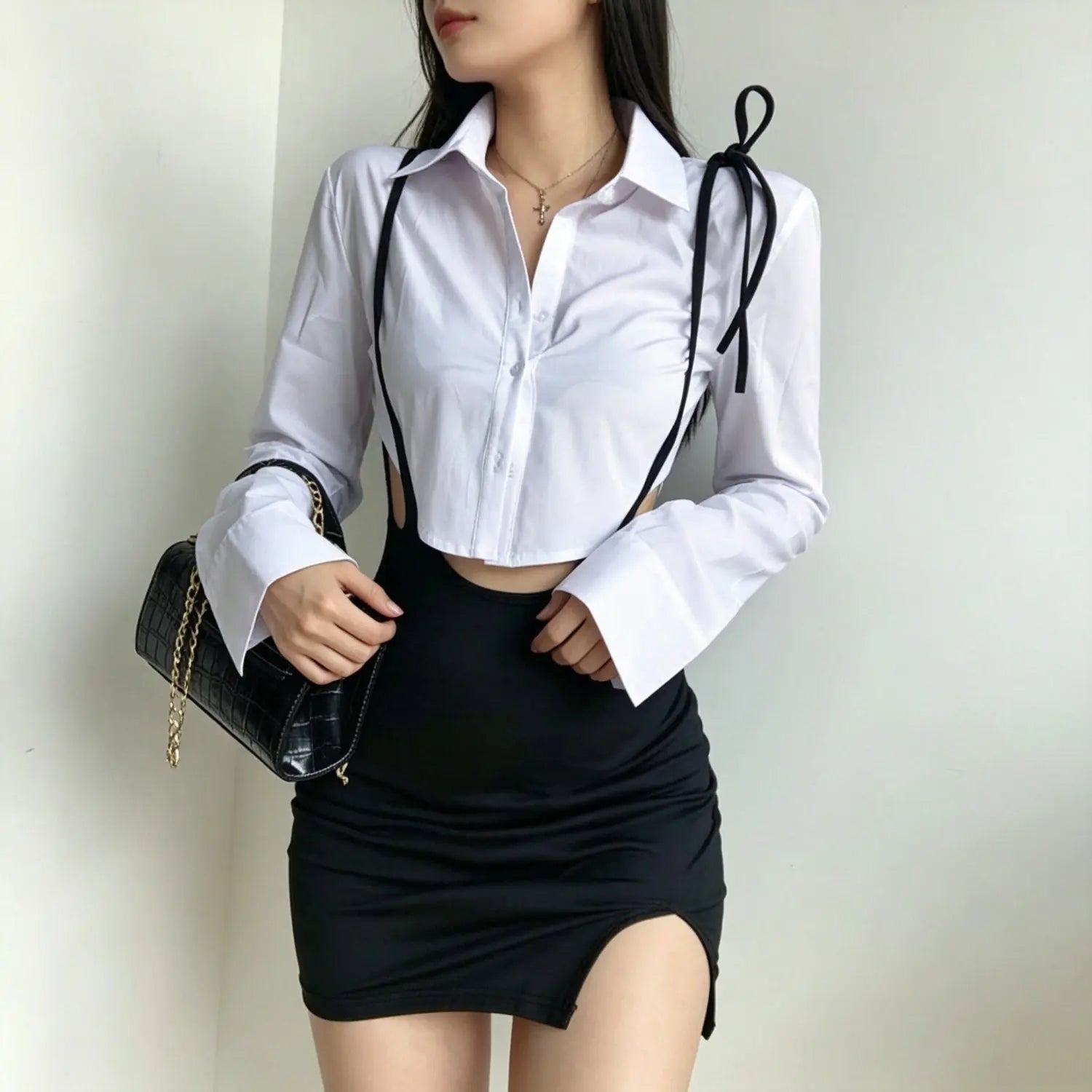 Front model pose of black tie‑suspender mini skirt with side slit and waist cutout detail