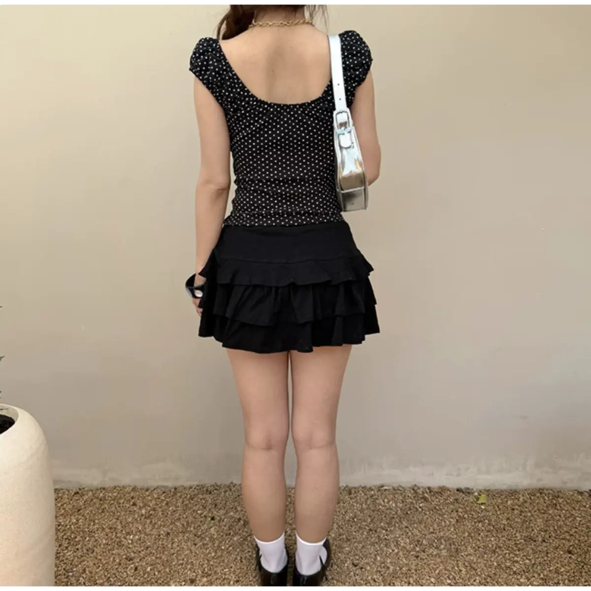 Back view of a black top with white heart prints, featuring cap sleeves and a scoop back, paired with a black ruffled mini skirt.
