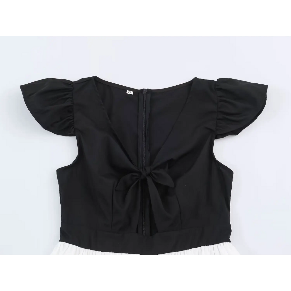 Back view of black peplum top with center zip, bow accent and white pleated hem