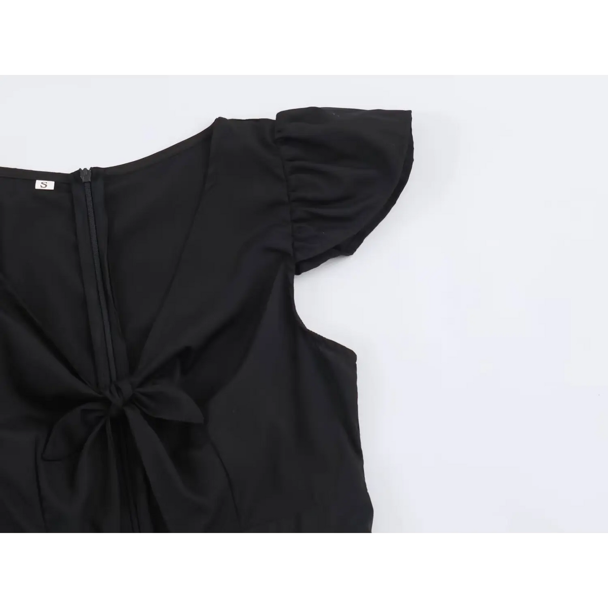 Close-up of back zip, black bow and ruffle cap sleeve on black white top with size S label