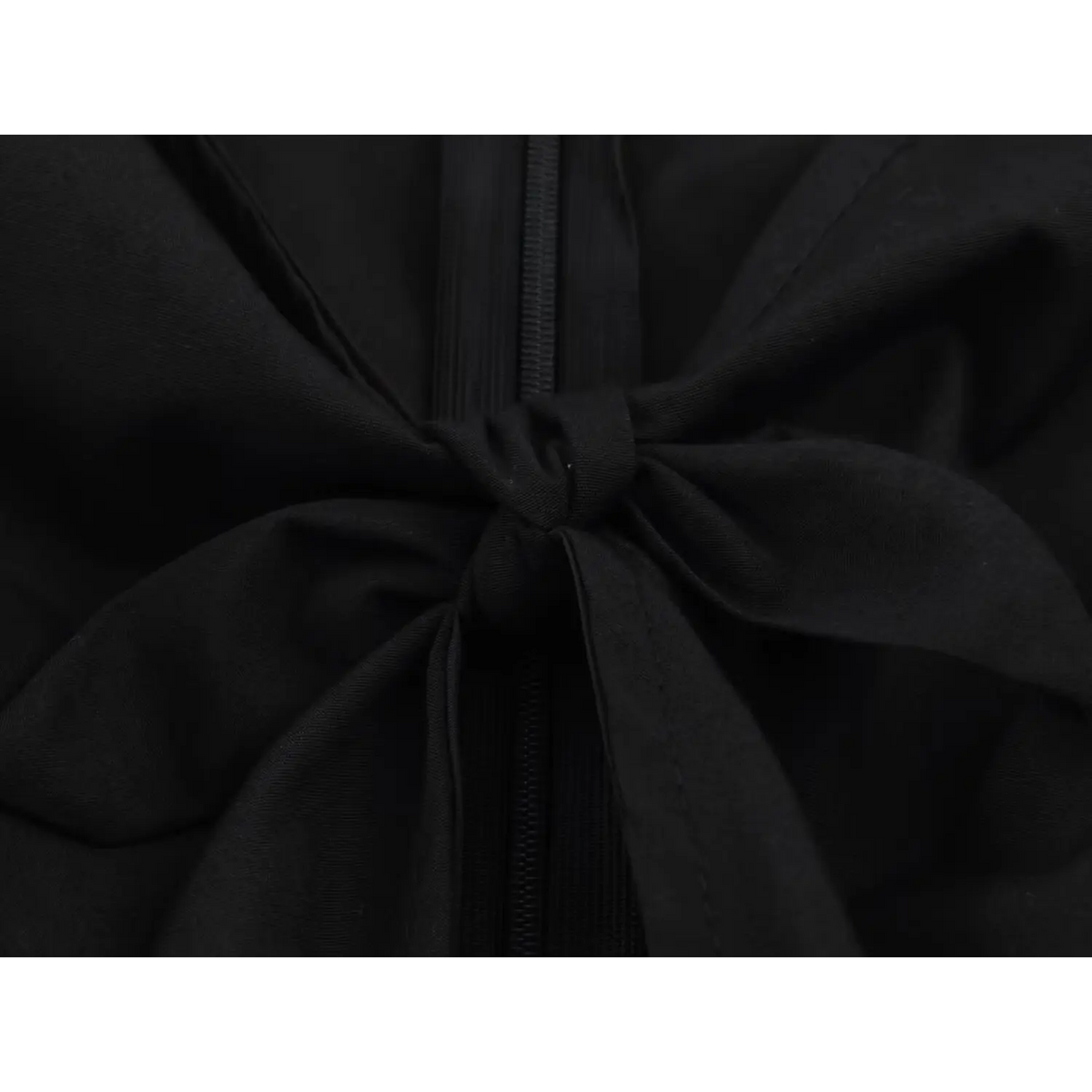 Close-up of fabric bow tied over zipper teeth on black peplum top