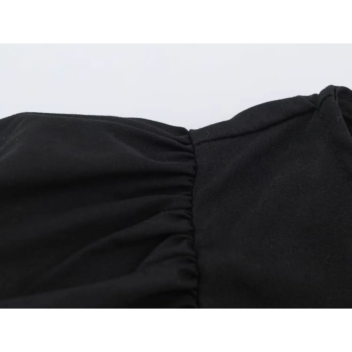 Close-up of shirred black fabric joined to smooth fabric panel on peplum top