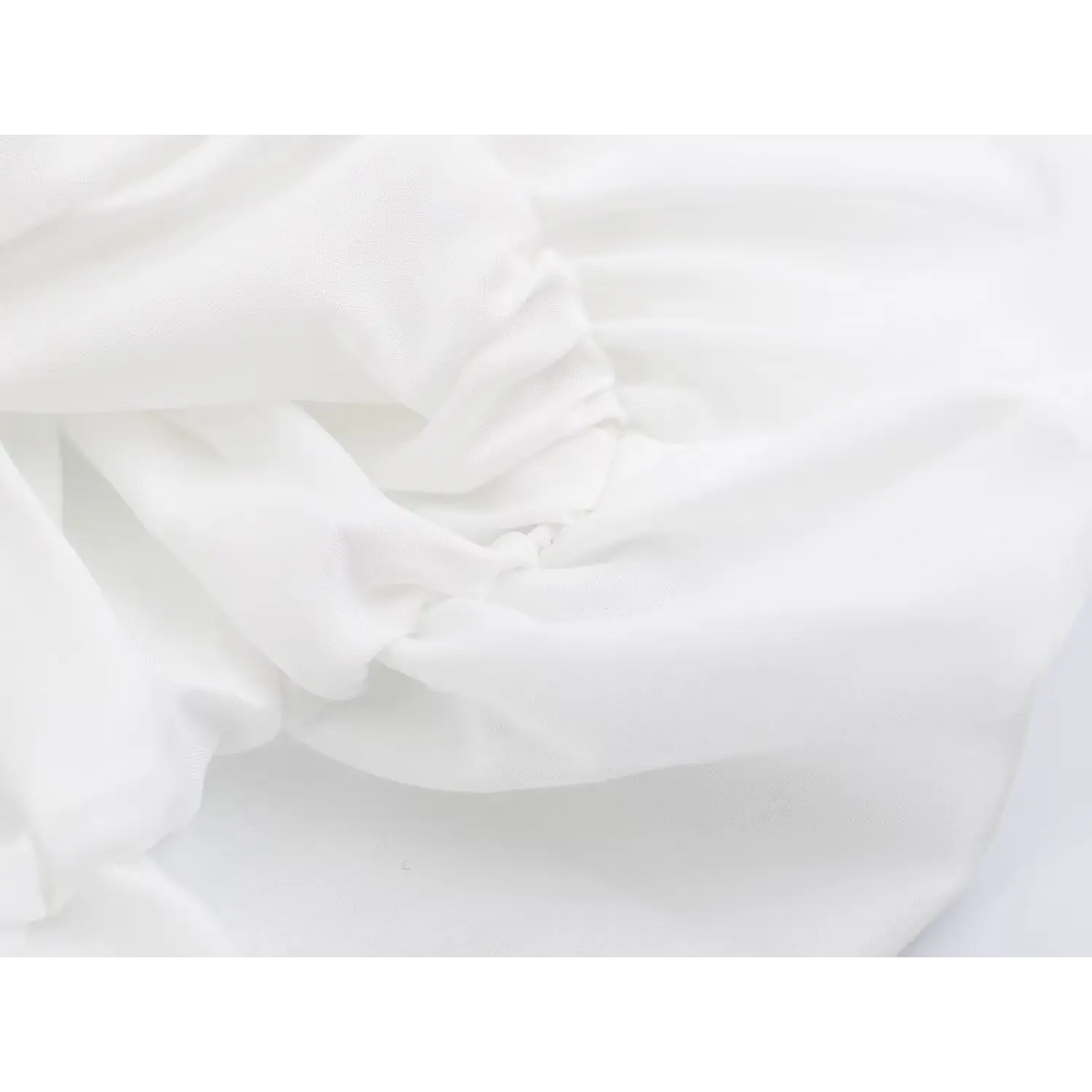 Close-up of softly gathered white fabric with stitched pleats on peplum hem