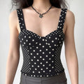 Model wearing a black and white polka dot bustier crop top with ruffled straps, styled with a black flower necklace and grey bottoms, front view.