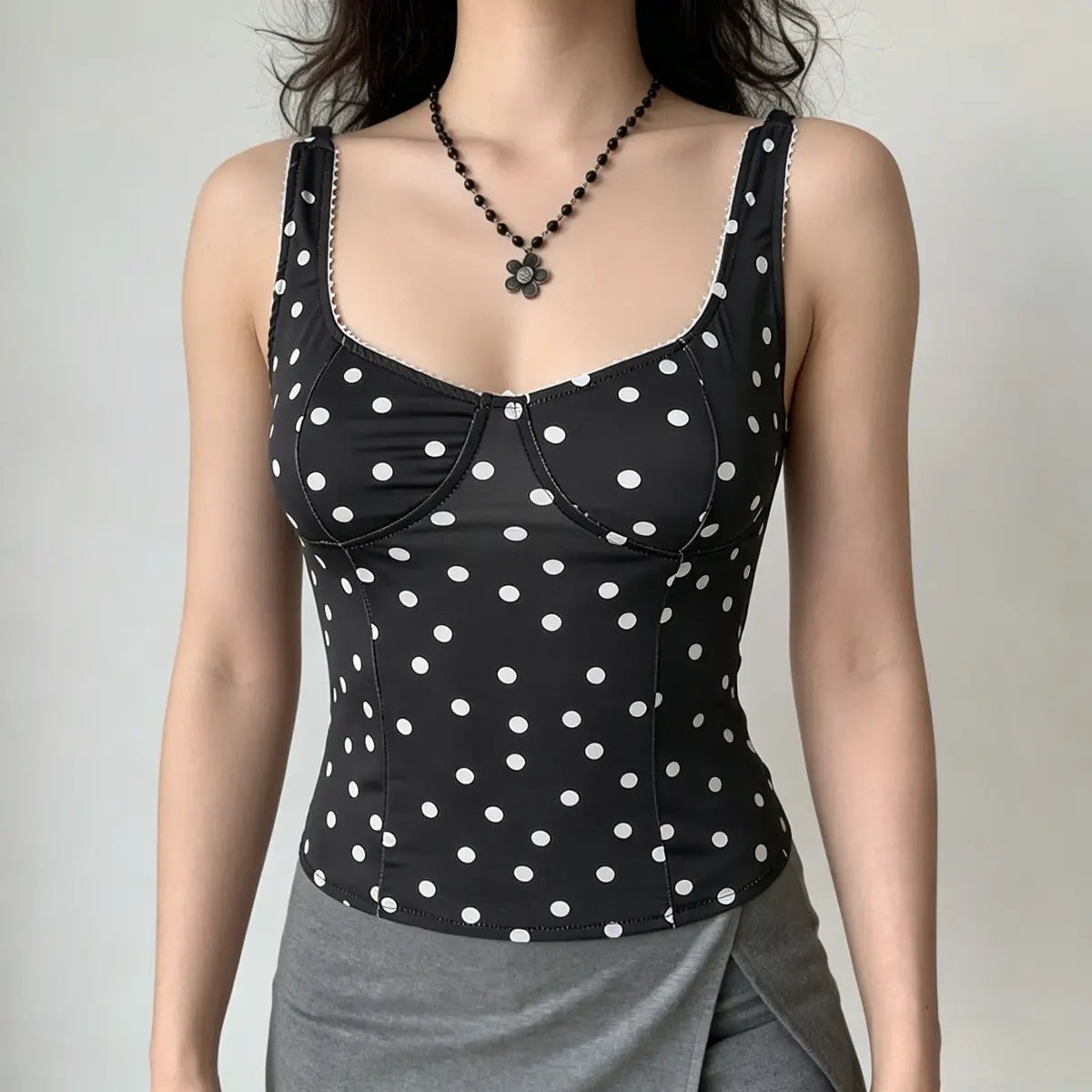 Model wearing a black and white polka dot corset-style camisole top with lace trim at the neckline, paired with a gray wrap skirt.