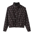 Black cropped windbreaker jacket with white polka dots, stand collar, front placket, side pockets, elastic cuffs, white background, flat lay front view