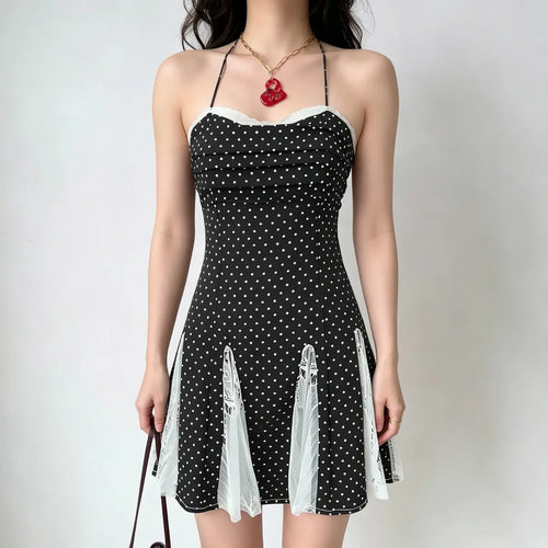 Model wearing a black and white polka dot halter-neck dress with lace panel details at the hem, carrying a brown handbag.
