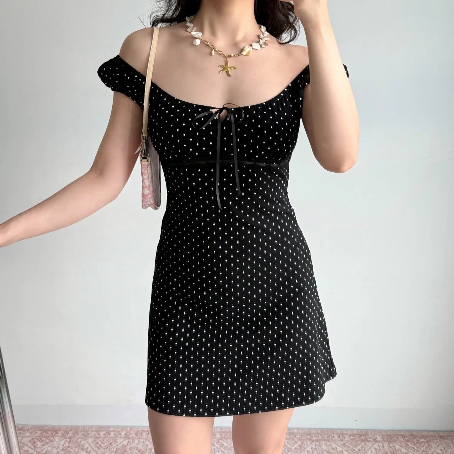 Model off‑shoulder front pose black white polka dot mini dress square neck ribbon tie lace detail cap sleeve bodycon dress