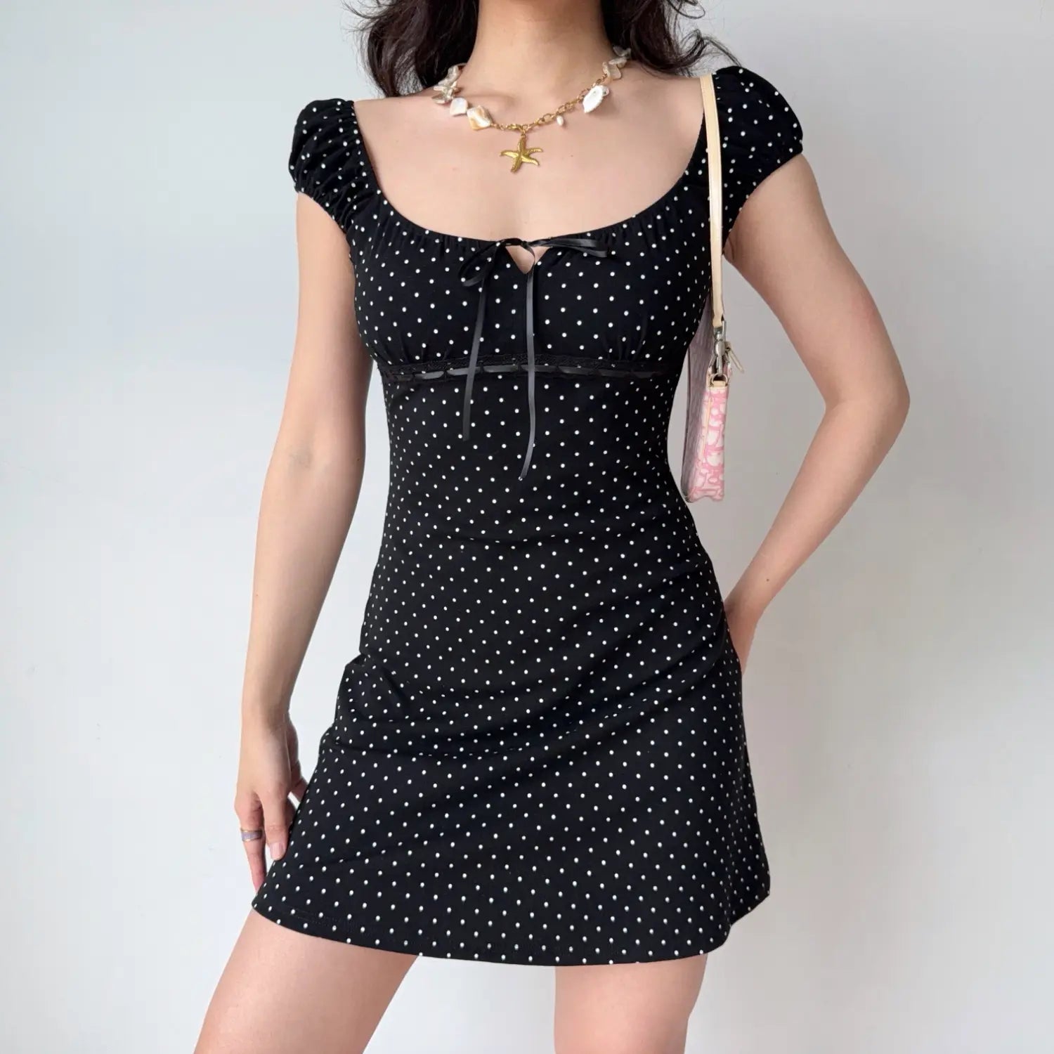 Model one hand behind waist pose black white polka dot mini dress fitted silhouette square neck ribbon tie detail