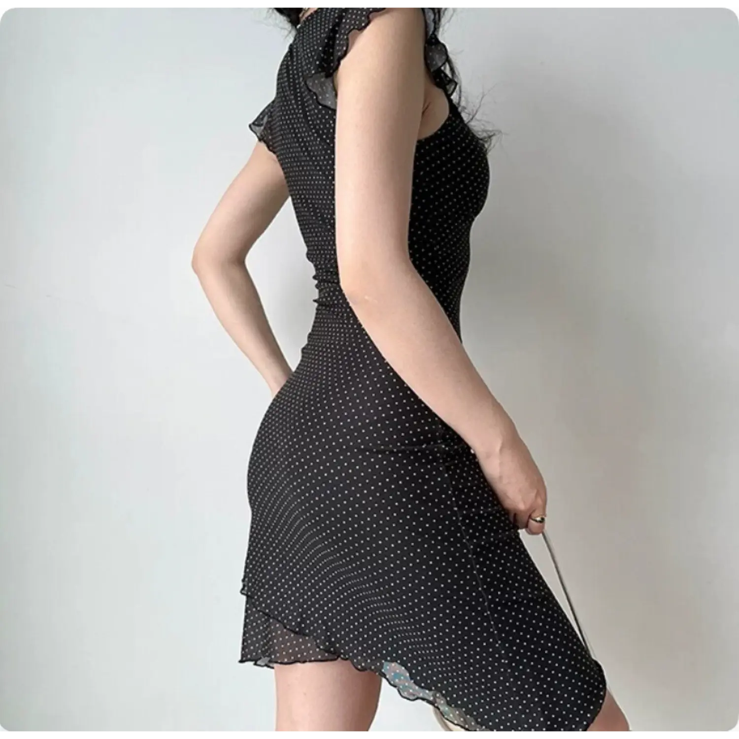 Side back view black mesh mini dress with white polka dots, ruffle cap sleeves, ruched bodycon asymmetrical hem