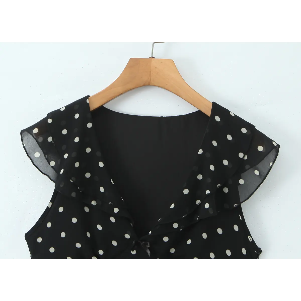 Close-up of the V-neckline with layered ruffled chiffon trim on the black polka dot dress.