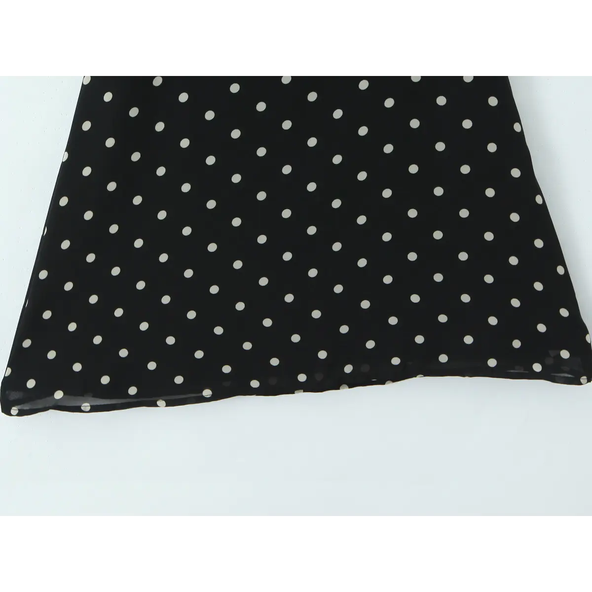 Close-up of the lightweight chiffon fabric and evenly spaced white polka dots on the black background.