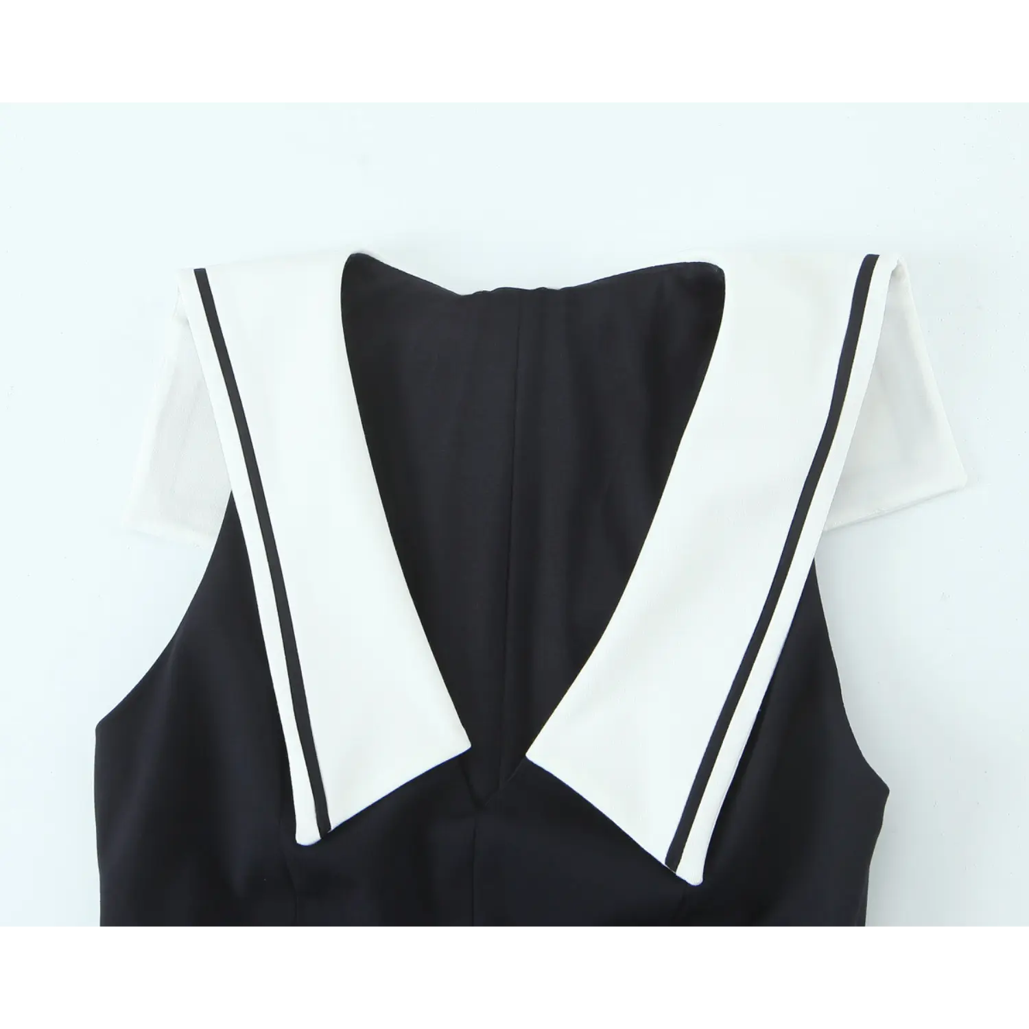 Close-up front V neck, wide white sailor lapel with single black piping edge, sleeveless cut, tailored woven black fabric