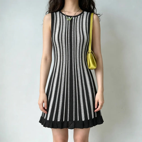 Model wearing a black and white striped knit mini dress with a ruffled hem, styled with a yellow handbag and green necklace, relaxed front pose.