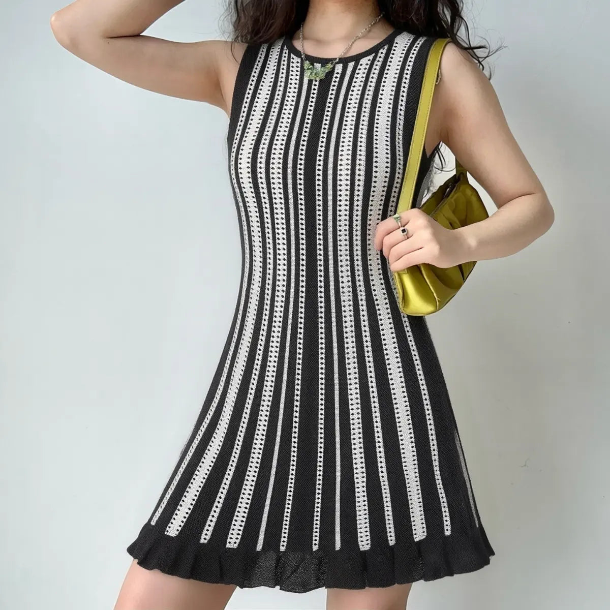 Model wearing a black and white striped knit mini dress, styled with a green bag, showing the form-fitting silhouette and flared skirt.