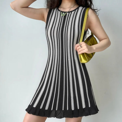 Model wearing a black and white striped knit mini dress, styled with a green bag, showing the form-fitting silhouette and flared skirt.