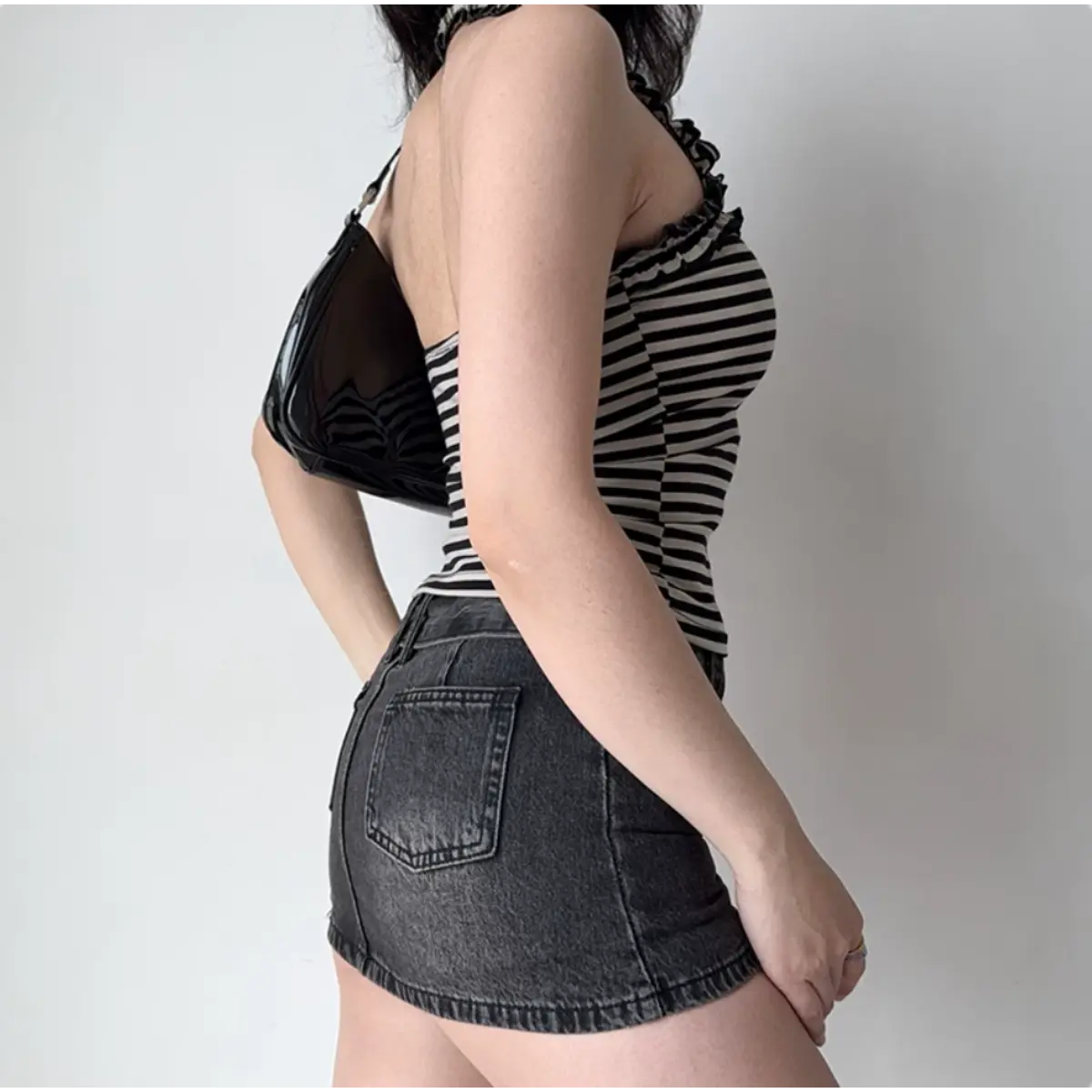Back view of a black and white striped halter top with ruffled trim, paired with a black denim mini skirt and a black shoulder bag.