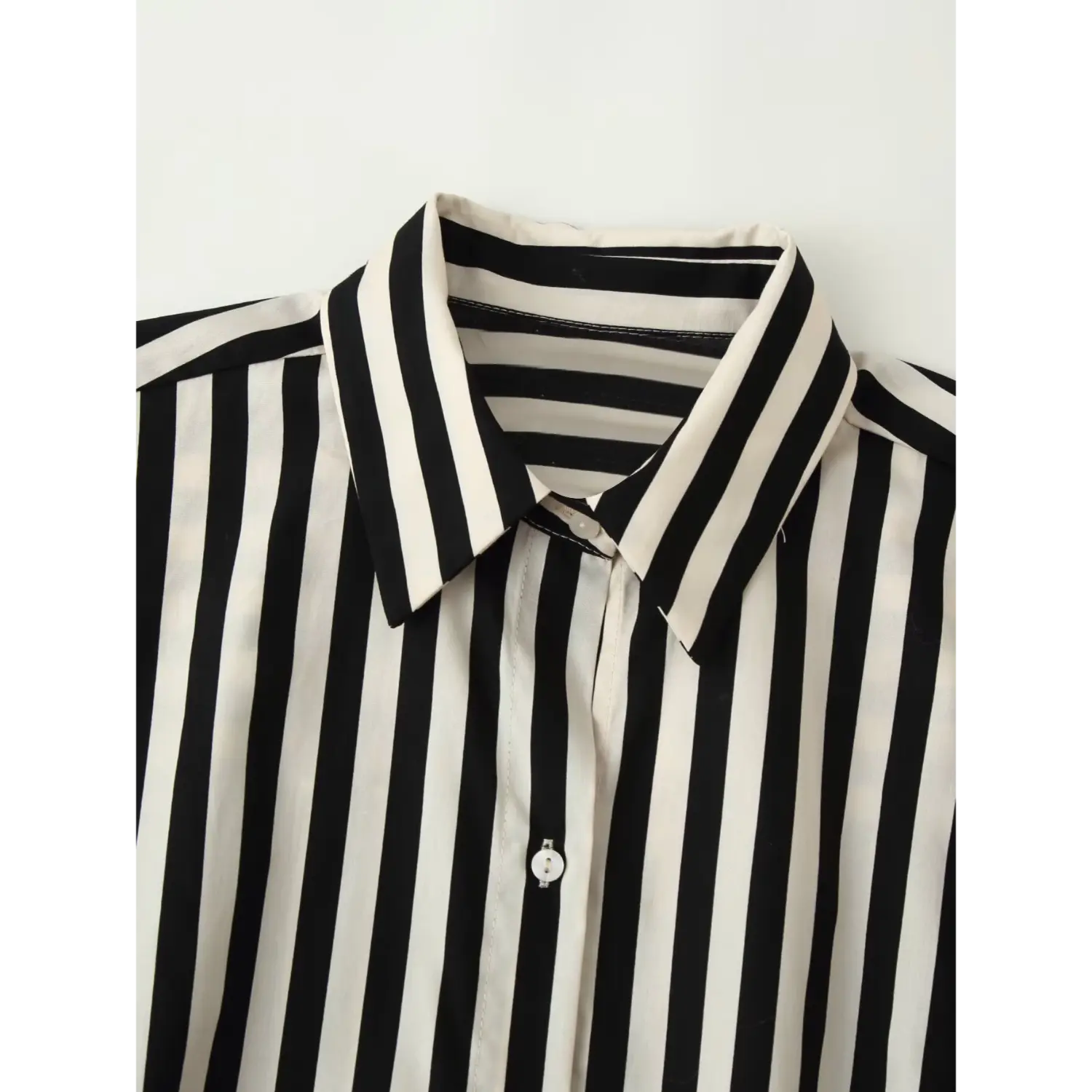 Close‑up of pointed shirt collar and front shell button, black‑off‑white vertical stripe woven fabric detail
