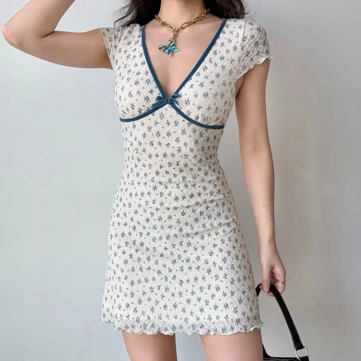 The white floral dress styled with a blue butterfly necklace, highlighting the V-neckline.