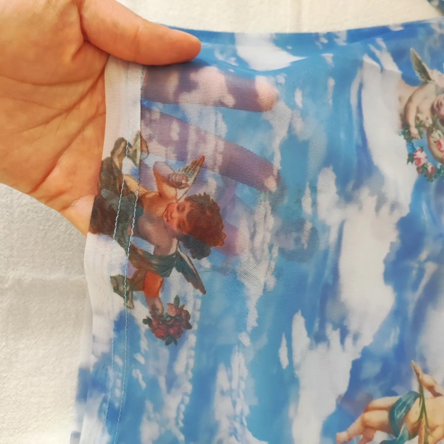 Close‑up side seam and sheer mesh fabric texture on blue cherub print turtleneck top