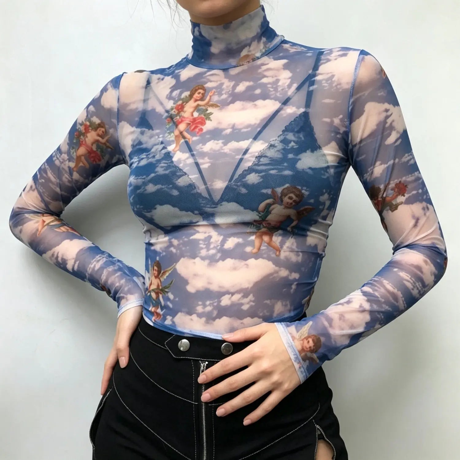Studio model hands‑on‑hips pose front view blue sheer mesh cropped turtleneck with cherub cloud print