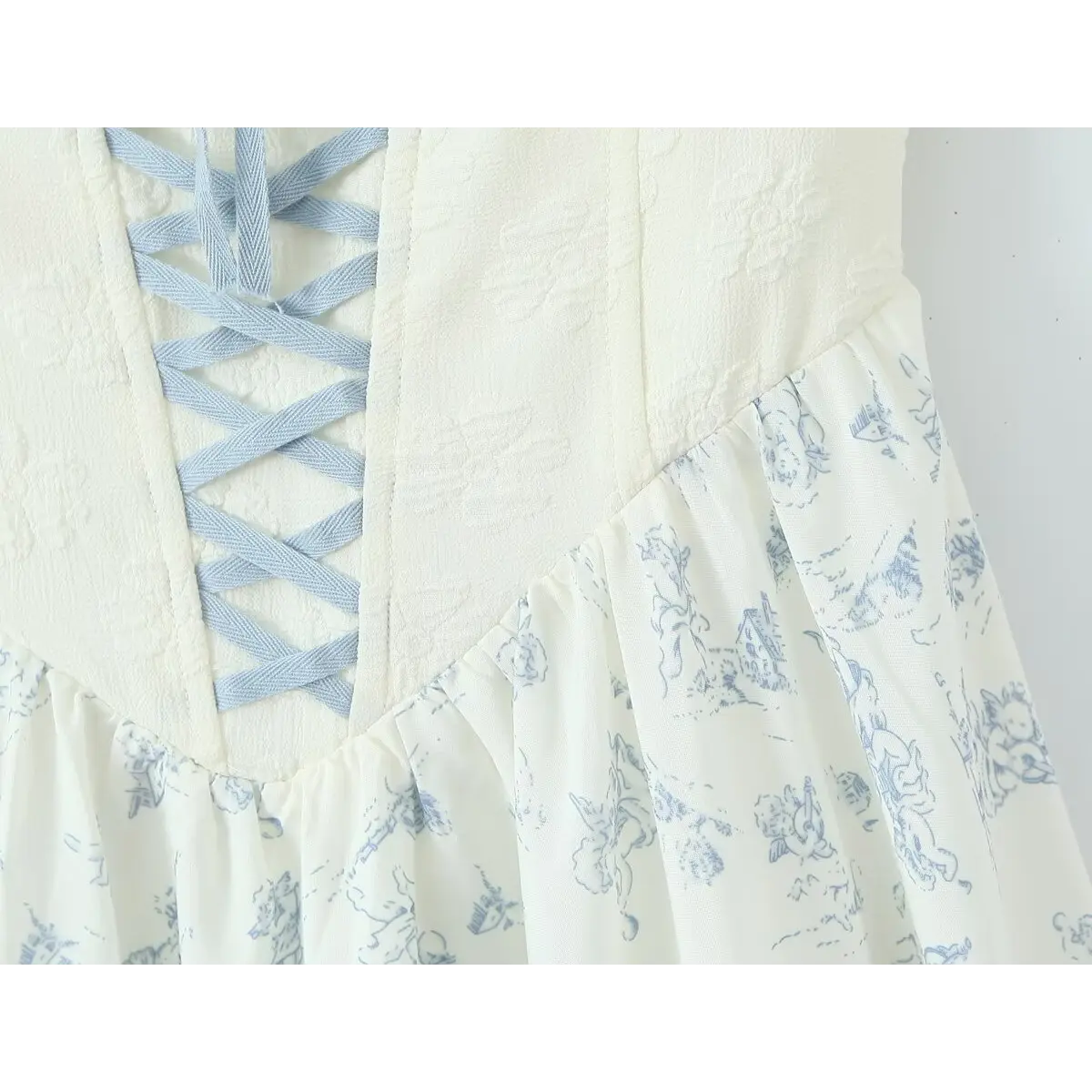 Close-up of the corset-style lace-up detail, showing the light blue crisscross ribbon on the textured white bodice and the gathered waist seam.
