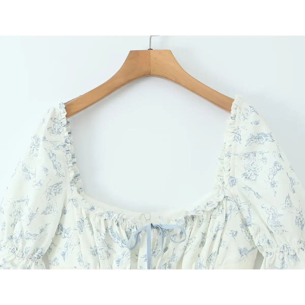 Close-up of the square neckline with ruffled trim and front blue ribbon tie.