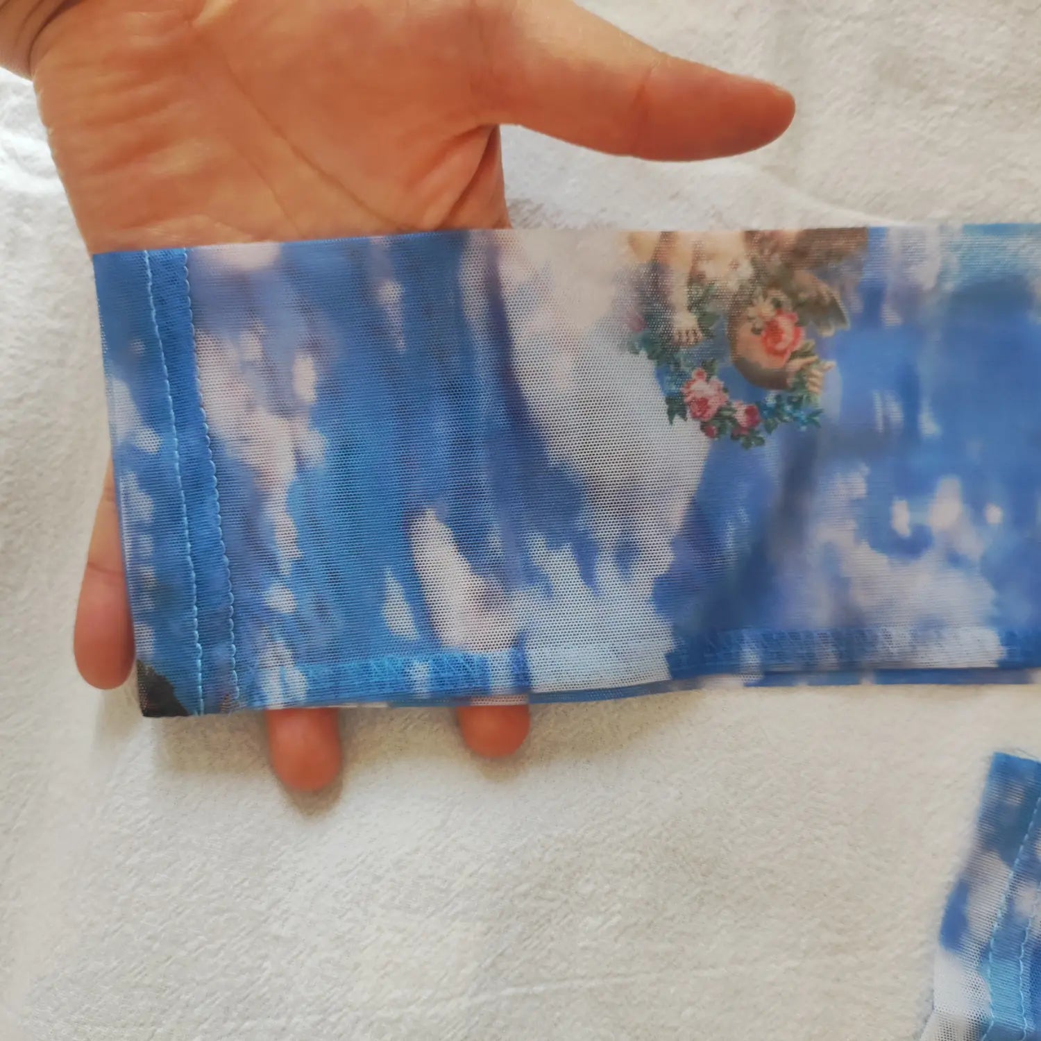 Close‑up sleeve cuff finished hem stitching on blue sheer mesh cherub sky print turtleneck top