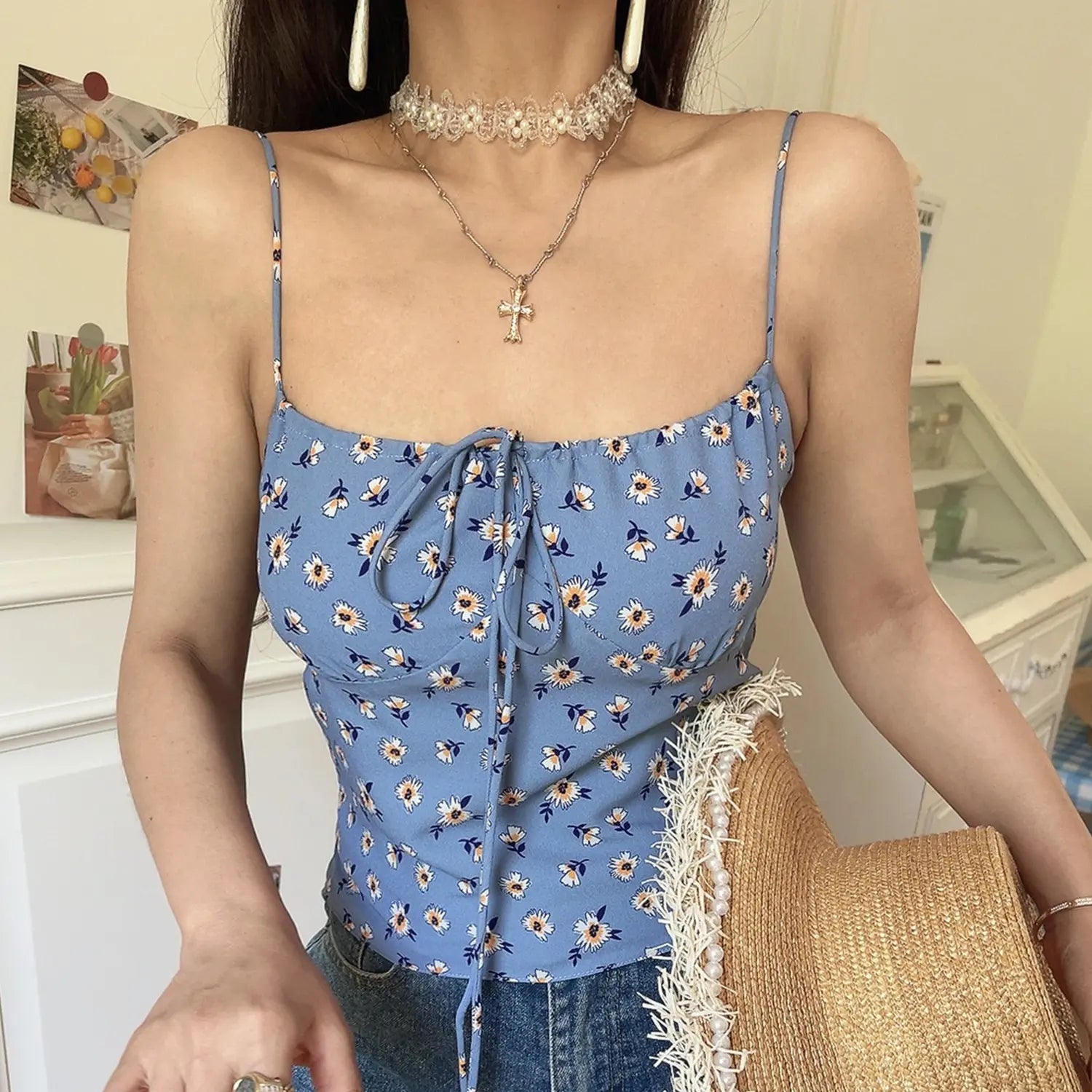 Haze blue base white yellow daisy cami crop top, adjustable front tie thin printed straps, full front model shot against white decor wall