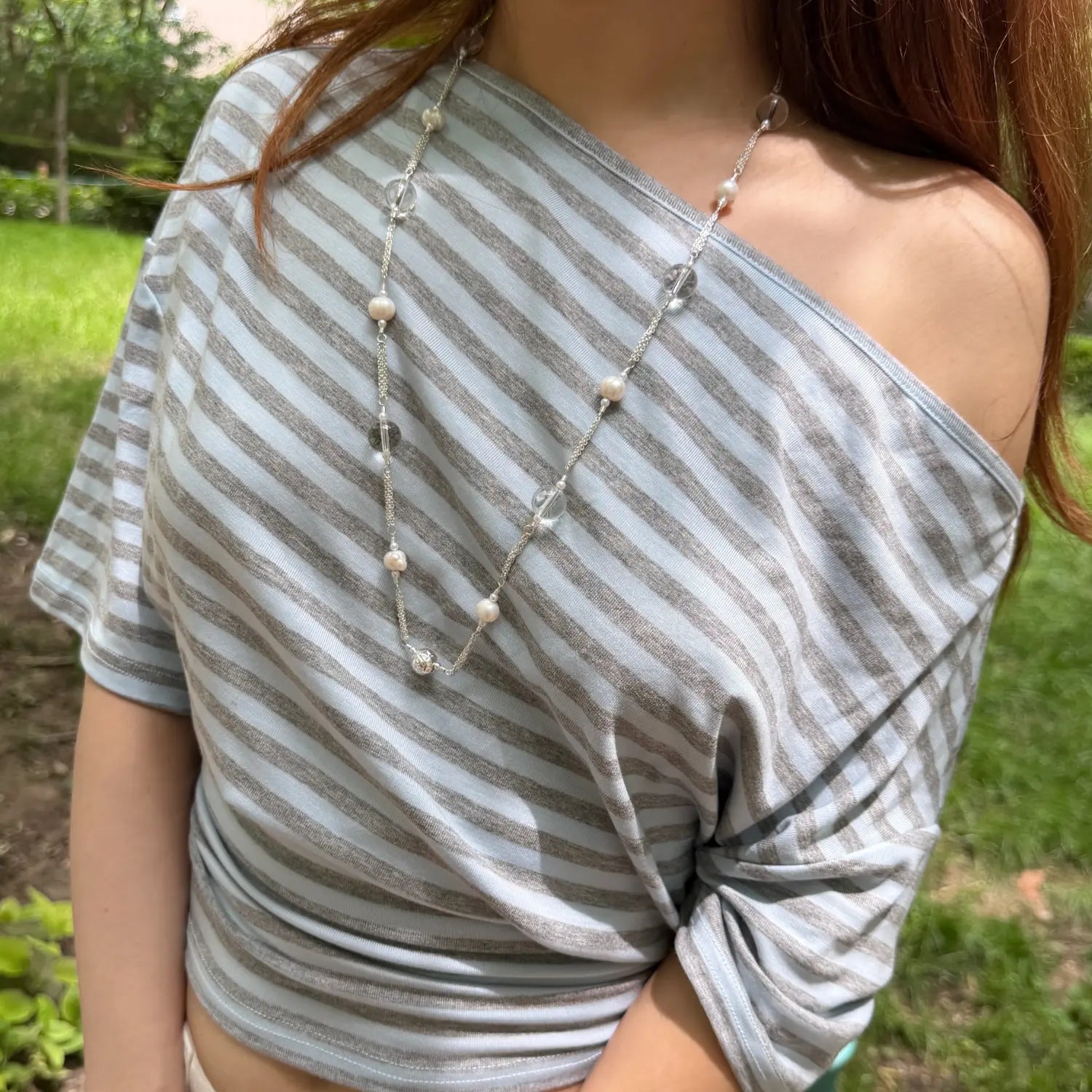 Close-up outdoor shot of striped off shoulder tee, horizontal blue grey stripe fabric, relaxed off shoulder neckline