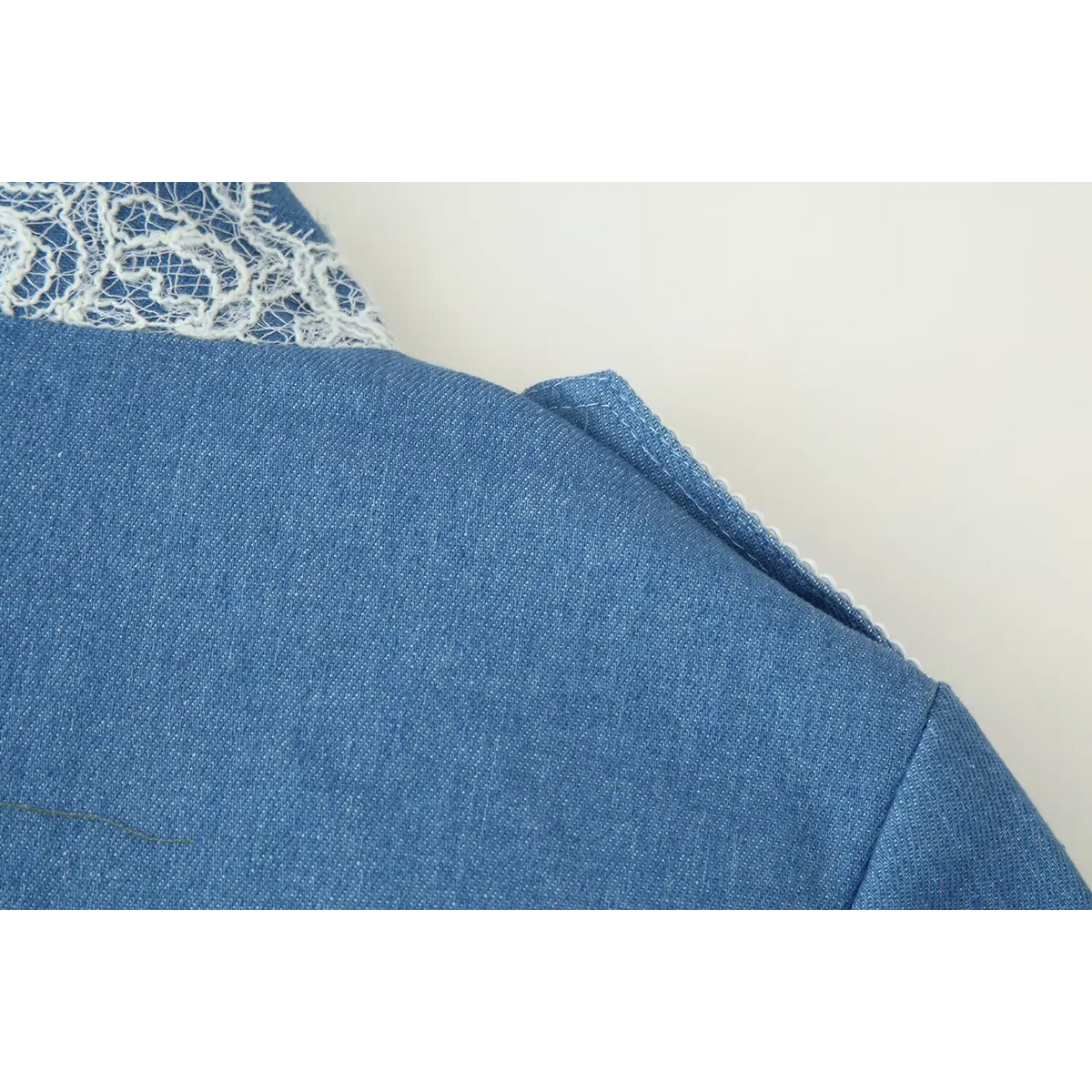 Close-up of shoulder seam and epaulet construction of blue cropped military style jacket