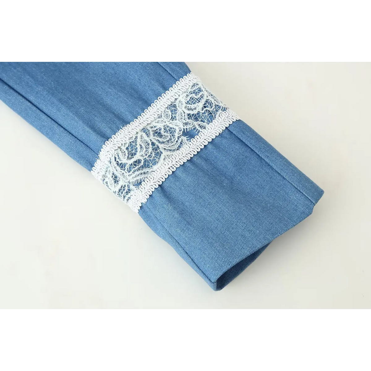 Close-up of sleeve cuff on blue cropped military jacket, decorated with ornate white floral eyelash lace trim