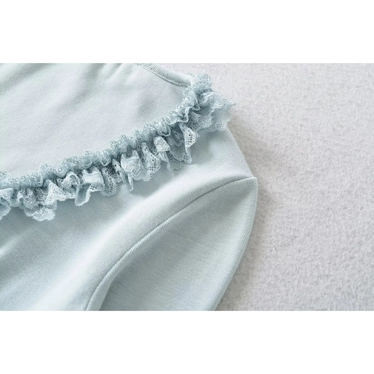 Closeup shot of lace ruffle trim on blue ribbed knit long sleeve top