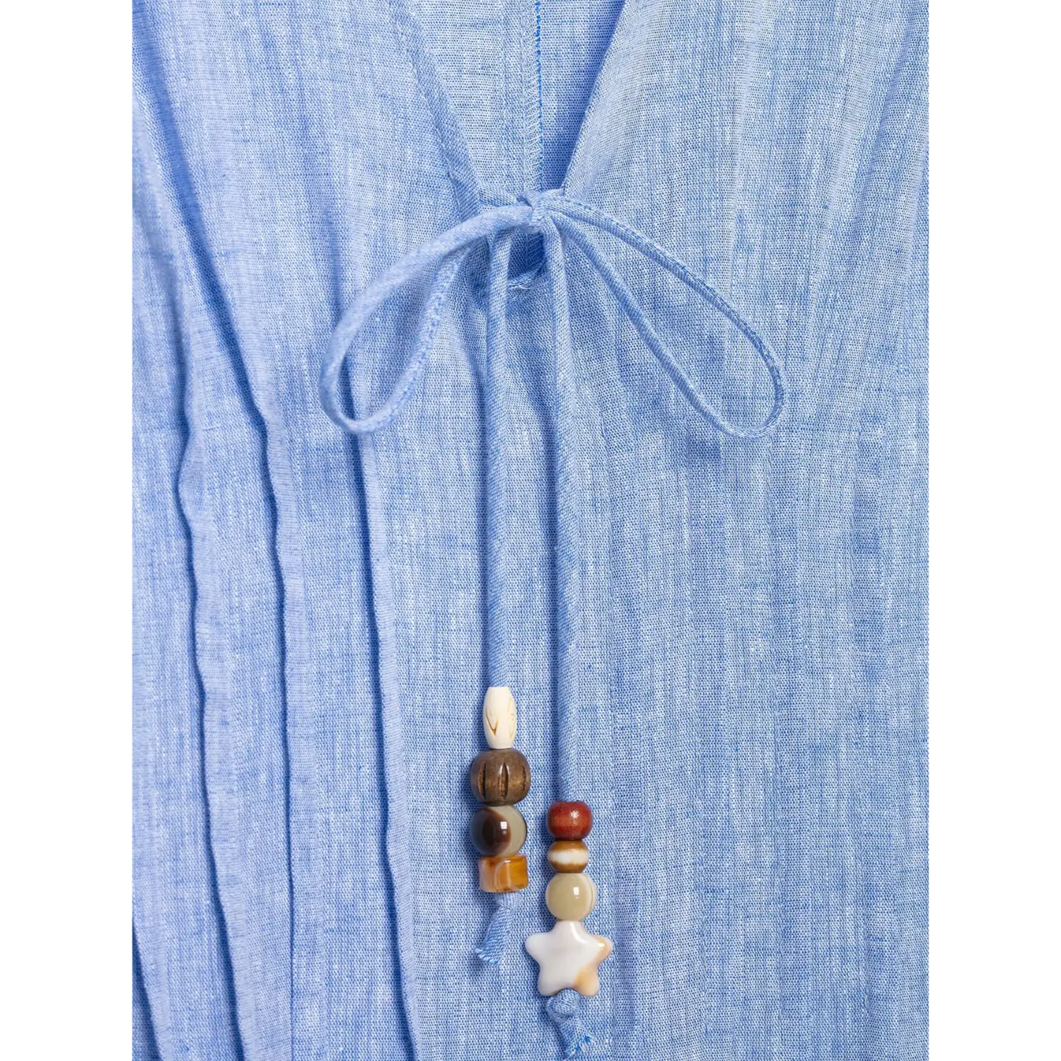 Macro shot v‑neck tie knot on blue linen dress, hanging mixed wooden and stone bead tassel decoration