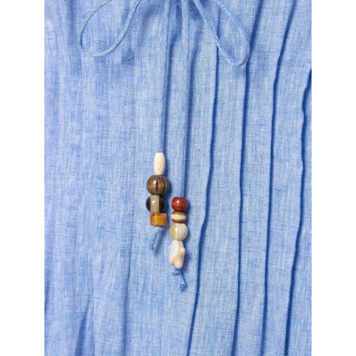 Detail shot bead tassel hanging on pleated blue linen fabric, natural linen texture