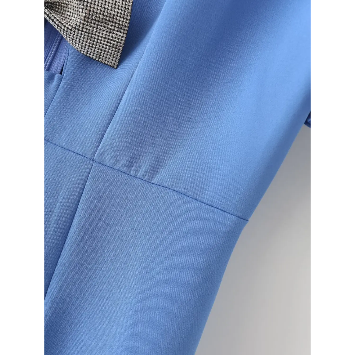 Close‑up tailored bodice vertical seam stitching, blue dress fabric partial rhinestone bow corner