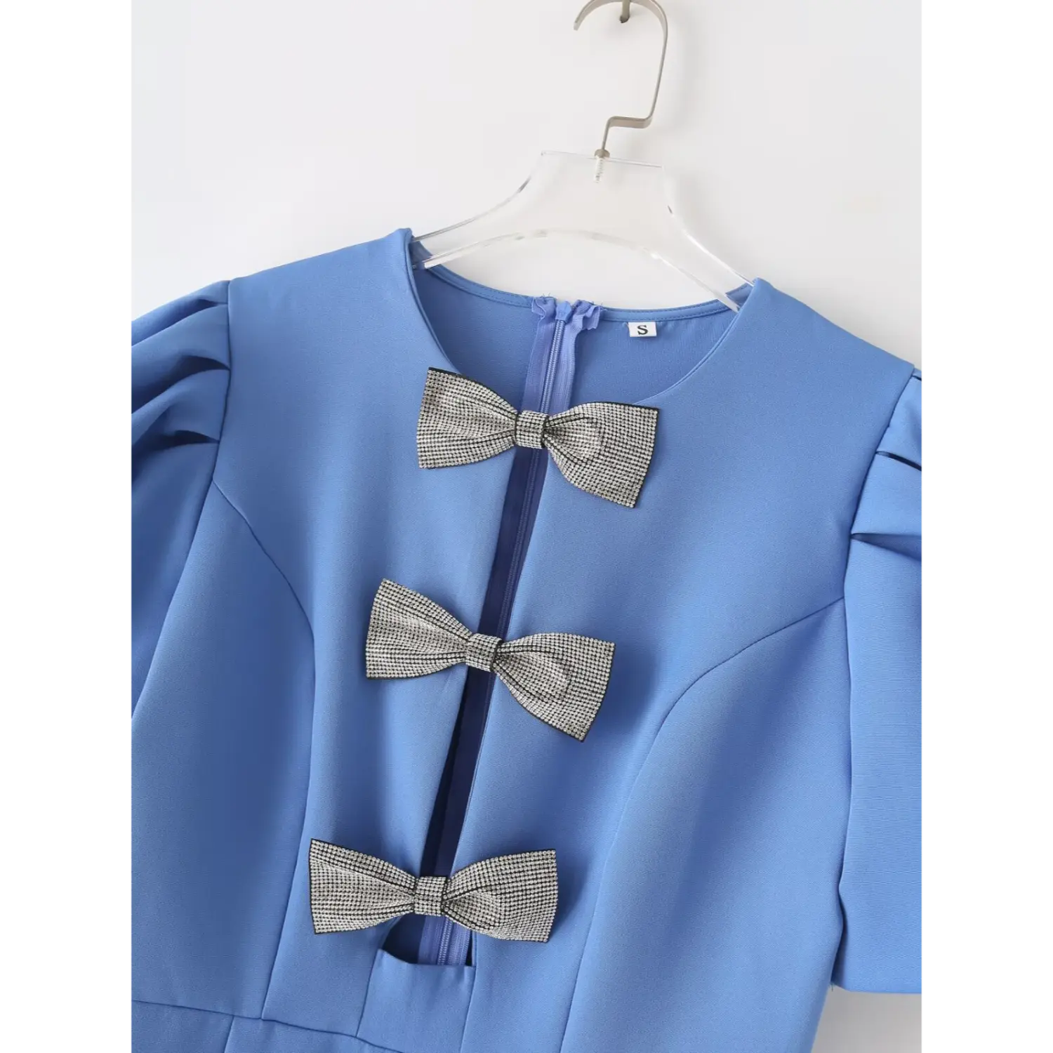 Close‑up bodice detail, three glitter rhinestone bows on blue mini dress, front keyhole cutout, inner zipper and size label