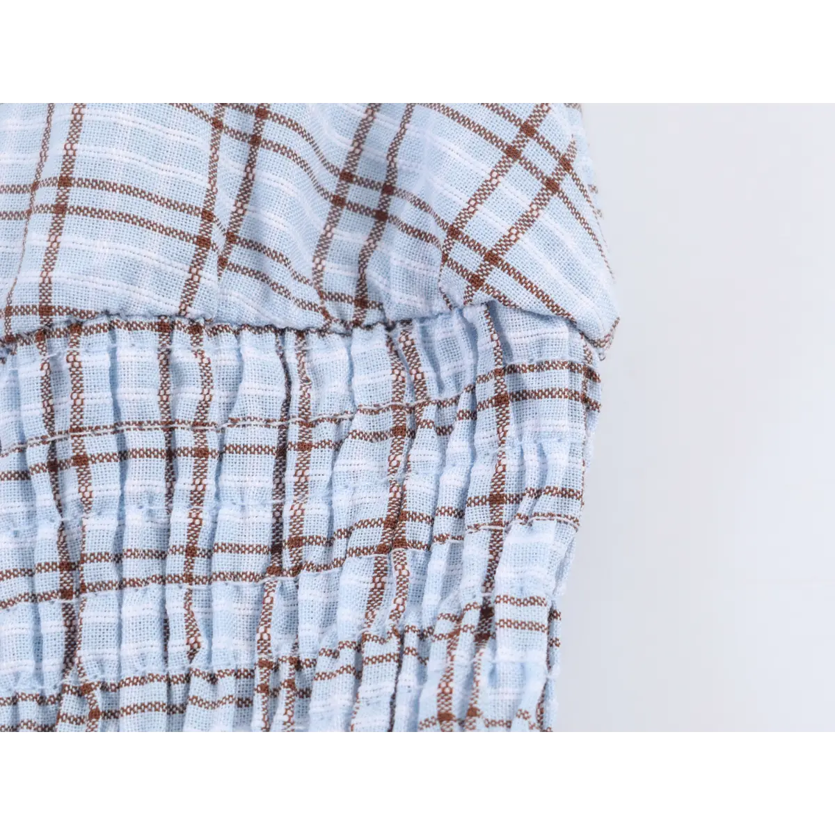 Close-up of the dress's smocked waist, showing the light blue and brown plaid pattern and textured fabric.