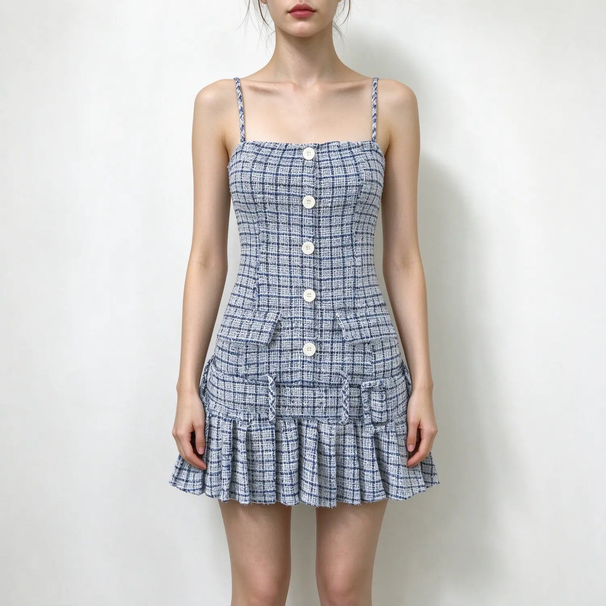 Model wearing blue plaid tweed spaghetti strap mini dress with front buttons and pleated hem, plain white background