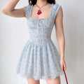 Model wearing cottagecore white mini sundress with light blue sketch rabbit and wildflower print, ruffled frill elastic shoulder straps, square neck self tie ribbon bow, fitted corset waist, flared A-line skirt with scalloped eyelet lace under hem, sweet casual summer streetwear outfit with chunky heart pendant necklace