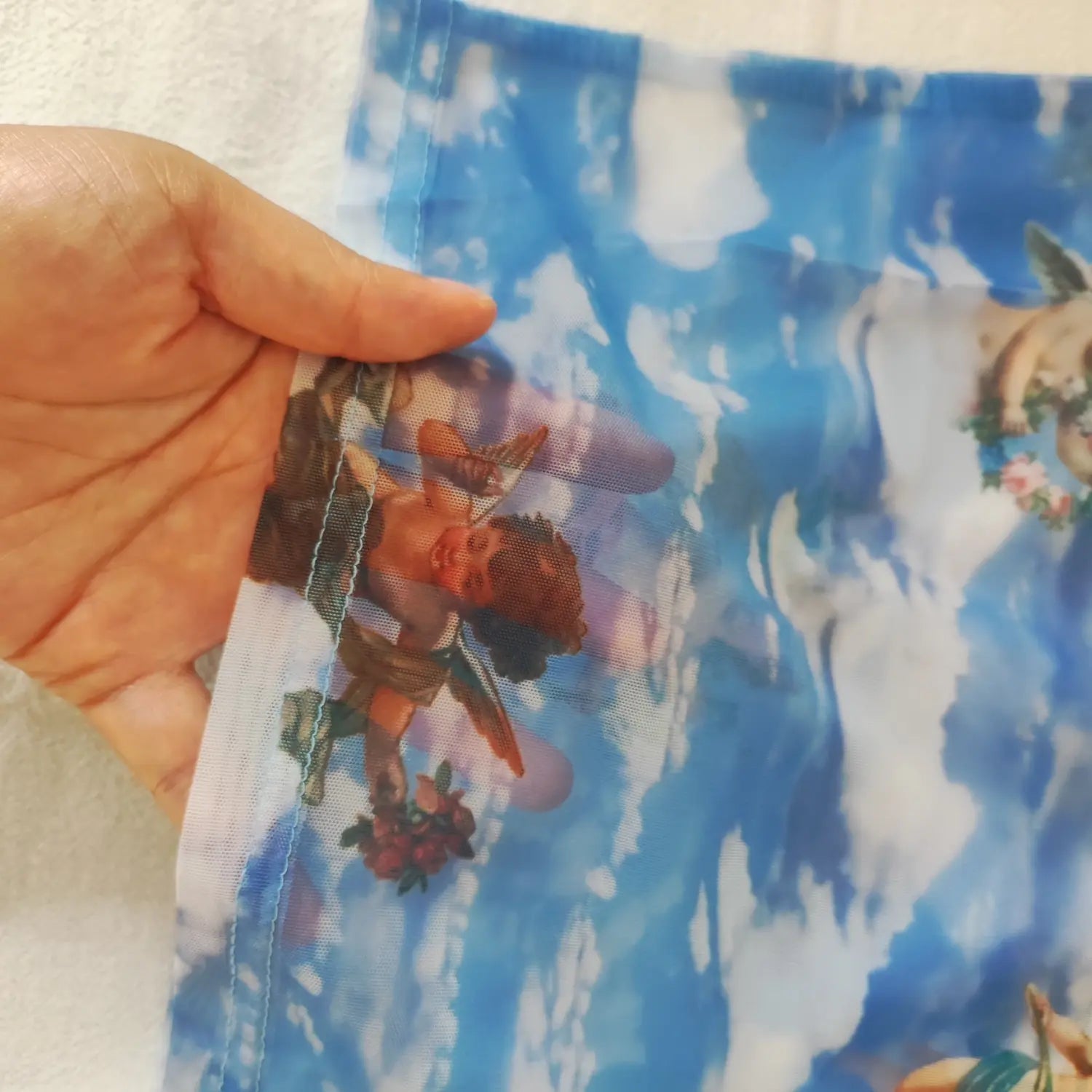 Hand‑stretched close‑up showing see‑through mesh texture and angel print detail