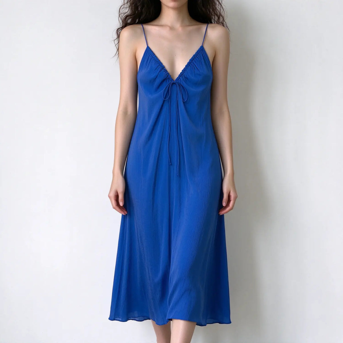 Model wearing blue spaghetti strap maxi dress, deep v neck, front tie detail, lightweight crinkle fabric, flowy loose silhouette