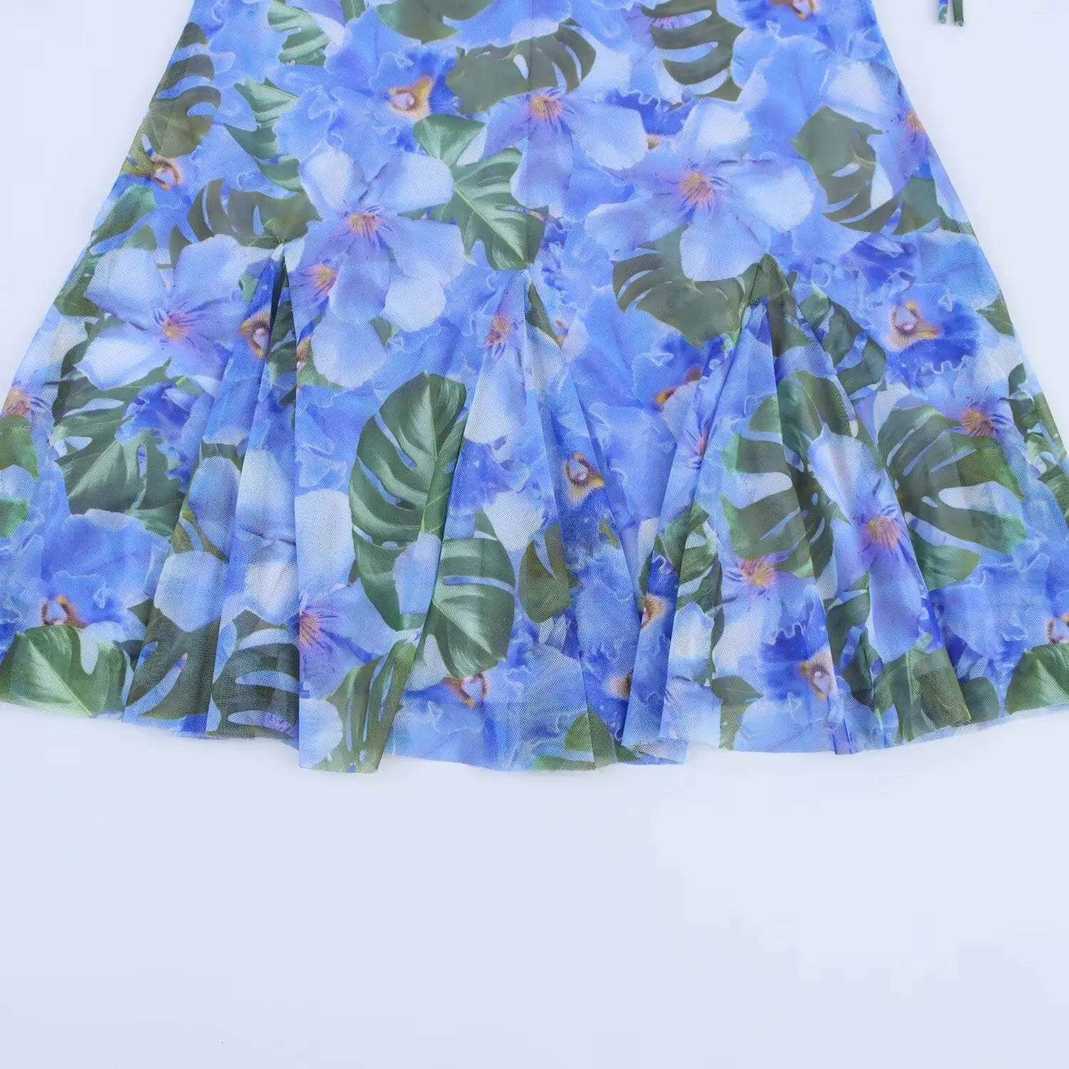 Flat close‑up of flared ruffle skirt hem, blue tropical flower and monstera leaf print mesh fabric