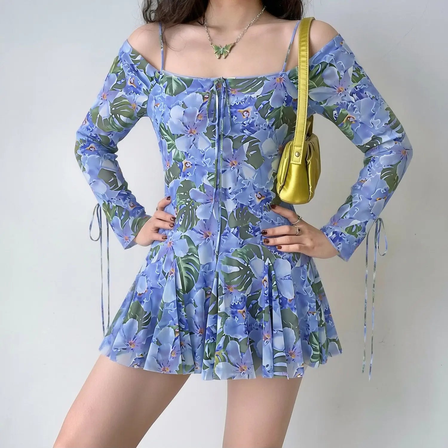 Model wearing blue tropical floral off‑shoulder long sleeve mesh mini dress, thin spaghetti straps, side sleeve drawstrings, flared ruffle mini skirt